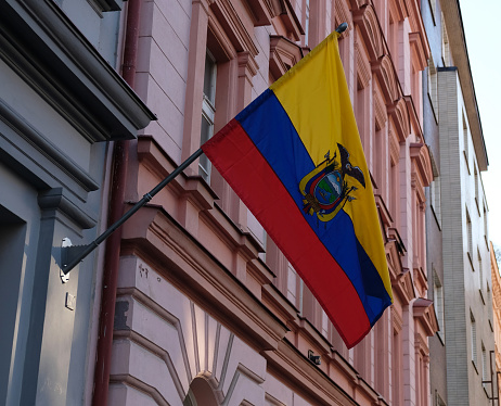 National flag of Ecuador, tricolor of yellow, blue and red, coat of arms with Condor. Ecuador flag on flagpole flutters in wind against of building of Embassy of Ecuador in Prague, Czech Republic.