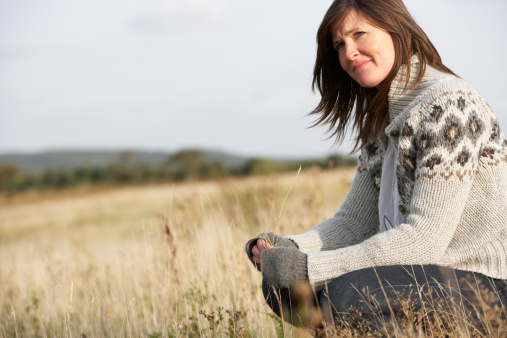 Young Woman Outdoors In Autumn Landscape sitting in a field looking into the distance