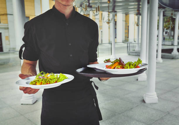 Waiter smiling while arranging sauces and appetizers on dining table in restaurant setting