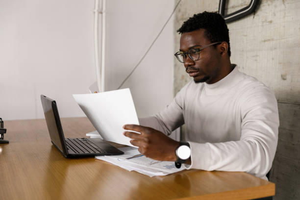 istock Diligent young businessman reviewing documents while working at his desk 1366012300