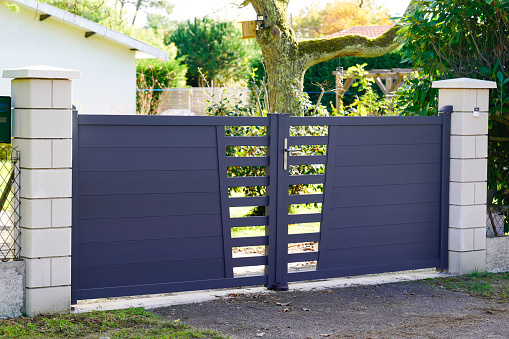 Metal driveway property entrance gates set in brick fence with garden trees  in background