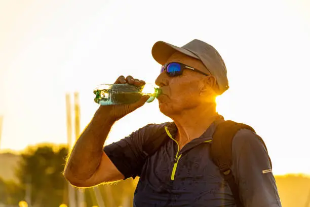 Photo of Active senior man, drinking water after he finished jogging at the marina during sunset