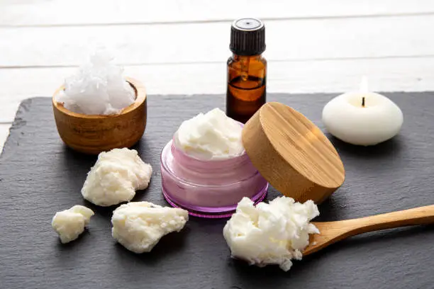 Photo of Making bodywhip also known as body butter, skin care moisturizer cream. Ingredients on wood background: shea butter,solid coconut oil, essential oils. Ready made body foam butter inside jar.