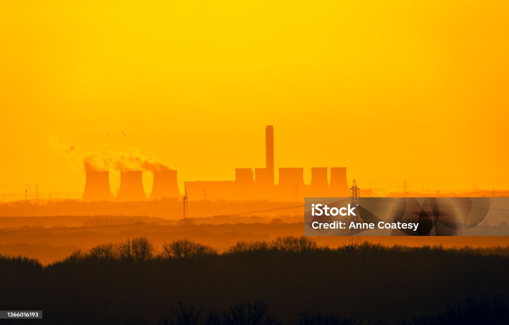 Distant view from the Yorkshire Wolds, UK of a Power Station's cooling towers near Drax in North Yorkshire. The sun is setting on a cold winter's night.  Wind turbines and electricity pylons in the background. Distant view from the Yorkshire Wolds, UK of a Power Station's cooling towers near Drax in North Yorkshire. The sun is setting on a cold winter's night.  Wind turbines and electricity pylons in the background.  Copy Space.  Horizontal. Carbon Capture Stock Photo