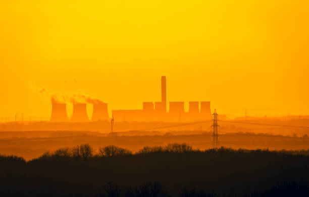 Distant view from the Yorkshire Wolds, UK of a Power Station's cooling towers near Drax in North Yorkshire. The sun is setting on a cold winter's night.  Wind turbines and electricity pylons in the background. stock photo