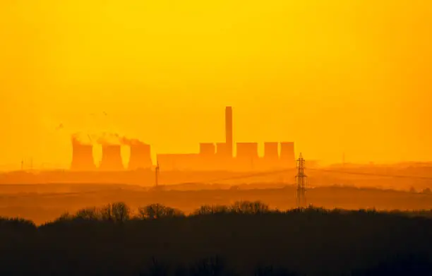 Distant view from the Yorkshire Wolds, UK of a Power Station's cooling towers near Drax in North Yorkshire. The sun is setting on a cold winter's night.  Wind turbines and electricity pylons in the background.  Copy Space.  Horizontal.