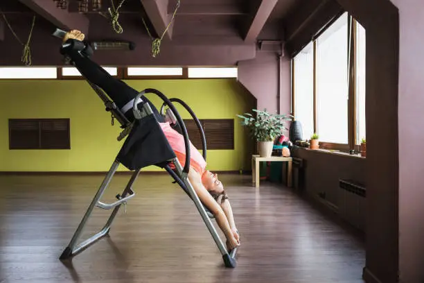 Photo of A woman doing inversion therapy hanging upside down on an inversion table, the therapy session is being done in a studio