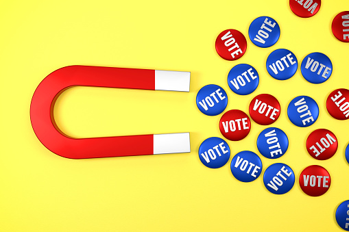 Metal Vote Badges Gravitated Towards a Red Magnet on yellow background. Insurance Concept.