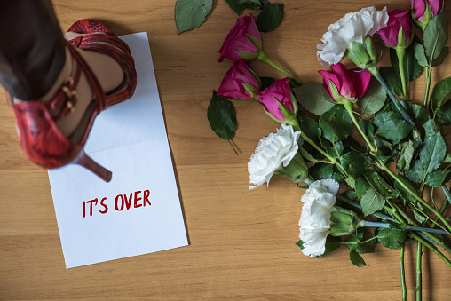 Woman legs in red high heel shoes standing on paper with word it's over on a floor with withered flowers. Heart broken concept. Divorce