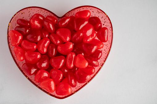 Heart shaped candy jelly beans in red heart bowl on white background