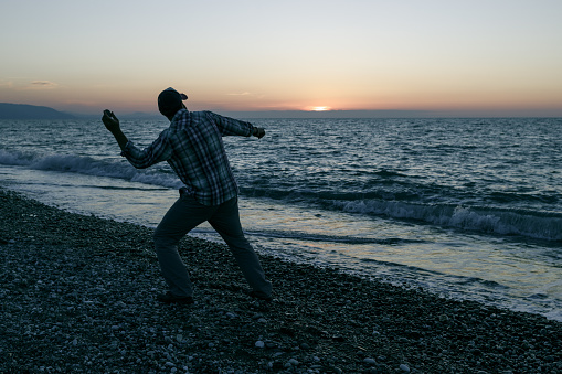 silhouette of a man who swings to throw a stone into the sea