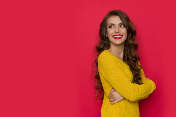 Beautiful smiling woman in yellow sweater is looking at red copy space. stock photo
