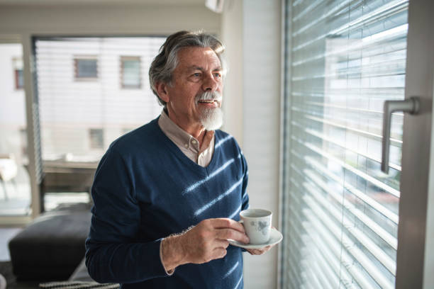 istock Mature old man drinking a cup of coffee by the window 1366034532