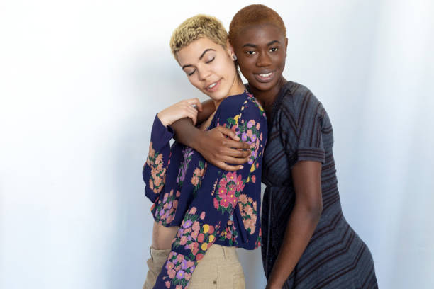 Multiethnic joyful women embrace and enjoy togetherness while looking at camera against background.