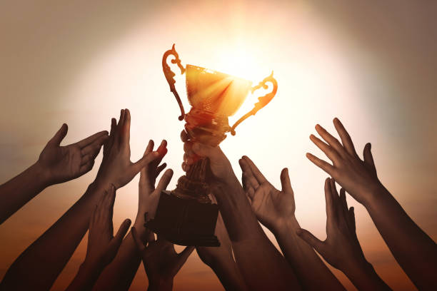 istock Winning team with gold trophy cup against shining sun in sky 1366042473