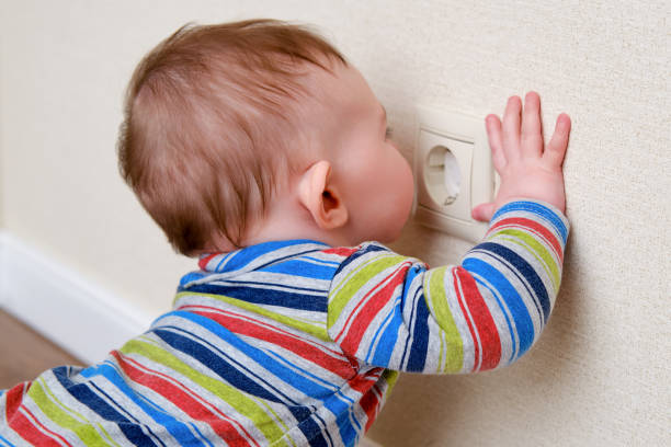 Baby toddler reaches into the electrical outlet on the home wall with his hand. Danger and protection of child fingers from electric shock Baby toddler reaches into the electrical outlet on the home wall with his hand. Danger and protection of child fingers from electric shock babyproof stock pictures, royalty-free photos & images