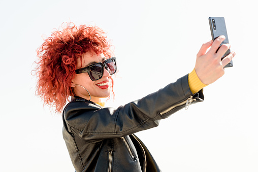 young latin woman with red hair makes a self portrait with her mobile phone from her vacations outdoors