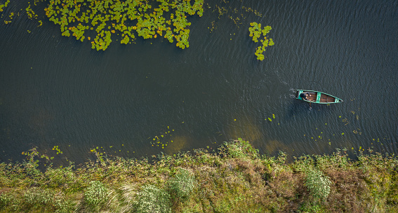 A man in a boat is fishing. Taken from a copter.