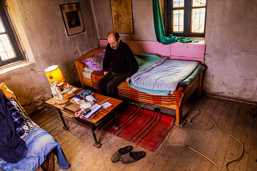 Homeless senior men, at the modest homeless shelter, sitting on the bed
