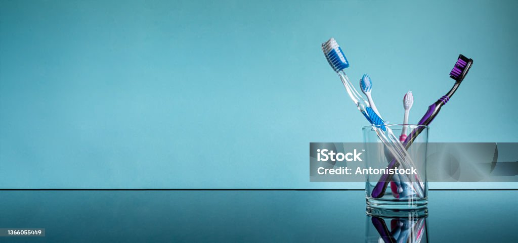 Different large and small toothbrushes for adults and children in a glass in the bathroom on a glass table with a reflection on a blue background. Toothbrush Stock Photo