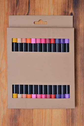 Set of sketching markers in a beautiful cardboard box packaging on a wooden texture background. Top view, close-up