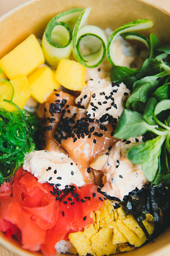 View of the colorful Hawaiian meal - Poke Bowl made from salmon, roce, vegetables and fruits, getting ready to taste it while staying home