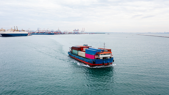 small container ship sailing in sea and shipping port background aerial view