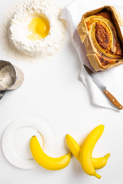 Banana bread on a white background with ingredients. Homemade delicious pastries. Top view, copy space.