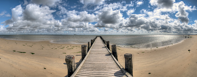Panoramic photo of a wooden jetty asu photographed at the Wadden Sea of the North Sea with cloudy sky above the Horizzont