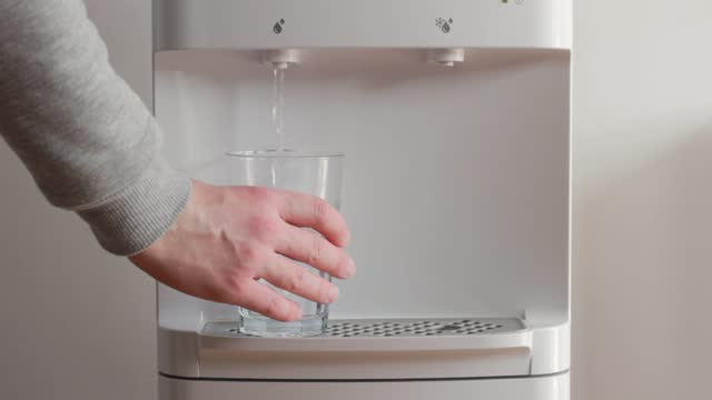 The man takes a glass of water from the water dispenser