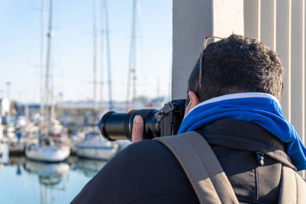 vista posteriore di un uomo che scatta foto in modo indiscreto con una fotocamera professionale con un obiettivo zoom - indiscreet foto e immagini stock