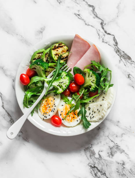 delicioso desayuno equilibrado, tazón de merienda - jamón, huevo duro, calabacín a la parrilla, ensalada verde en un tazón sobre un fondo claro, vista superior - salad breakfast cooked eggs fotografías e imágenes de stock