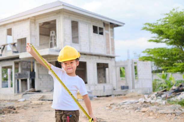 bambino asiatico che indossa un cappello rigido di sicurezza che tiene il nastro di misurazione in piedi di fronte al cantiere - little boys measuring expressing positivity intelligence foto e immagini stock