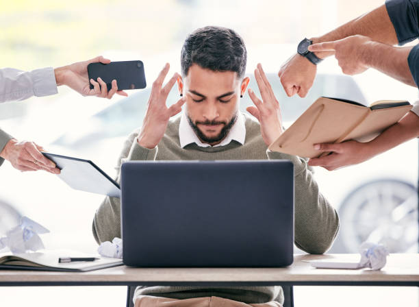 tiro de um belo jovem empresário sentado no escritório e sentindo-se estressado enquanto seus colegas colocam pressão sobre ele - telephone hysteria business men - fotografias e filmes do acervo