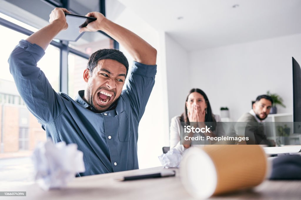 Shot of a handsome young businessman sitting in the office and breaking his digital tablet in anger How dare you freeze on me! Shouting Stock Photo