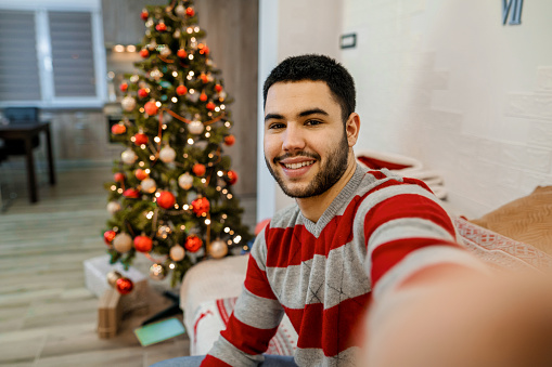 Happy young man taking a selfie during Christmas in the living room
