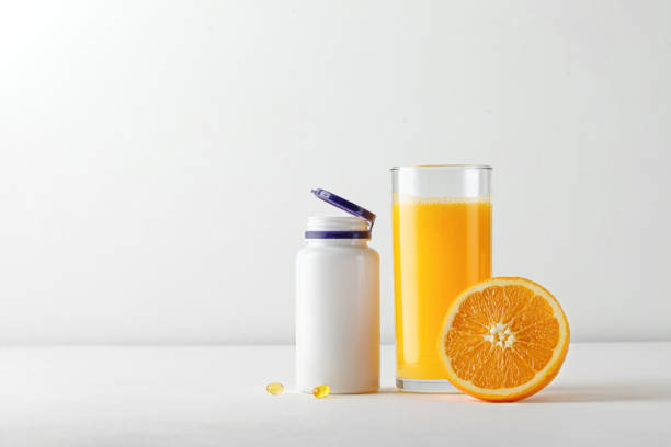 jugo de naranja fresco en un vaso y botella de vitaminas sobre mesa blanca. hipovitaminosis - vitamin pill vitamin c nutritional supplement bottle fotografías e imágenes de stock