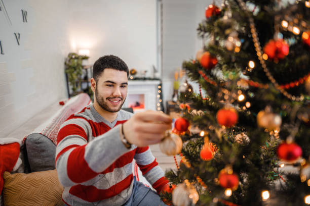 istock Young men decorating Christmas tree in the living room 1366078272