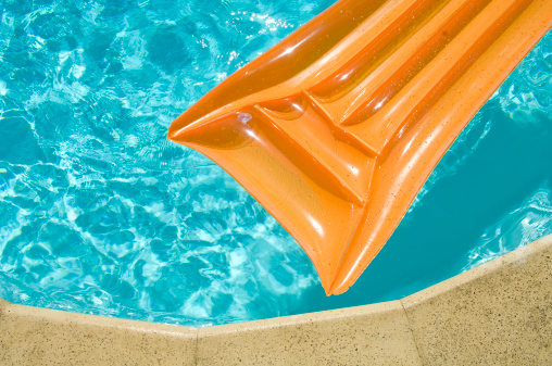 Orange inflatable bed at the edge of a swimming pool on a hot summer's day