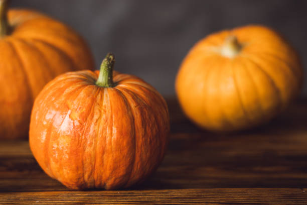 istock Three orange pumpkins on the brown table and grey background. Selective focus 1366083138