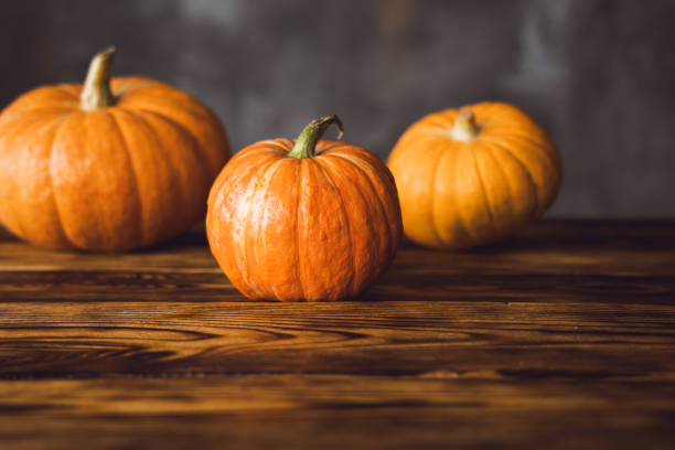 istock Three orange pumpkins on the brown table and grey background. Selective focus 1366083211