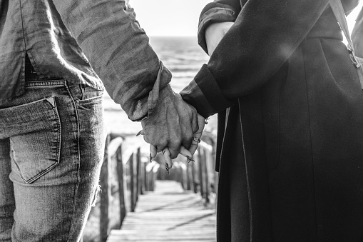 Closeup of young couple holding hands walking down on wooden stair towards the beach - Hipster couple, holding hands, in love enjoying romantic evening at beach - Female hand with beautiful long nails