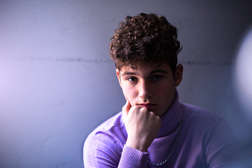 Copy-space. Selective focus. A young boy with curly hair in a retro outfit is sitting and watching in front of him. He is wearing a purple turtleneck sweater and a silver necklace.