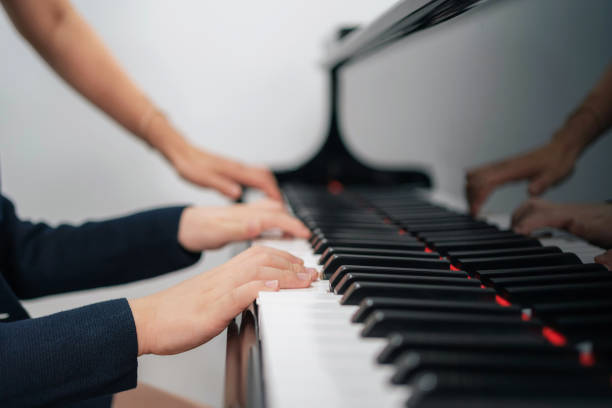 istock Selective focus on the kid finger playing grand piano. Teacher or instructor teach a boy on the class play melody. Close up hand of child. Music with piano. Education and learning concept.