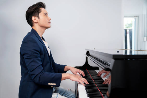 un hombre confiado vestido con traje azul y jean sentado en la silla y tocando el piano de cola con fondo blanco. esperando. músico toca melodía. retrato y concepto de estilo de vida - pianist grand piano piano playing fotografías e imágenes de stock