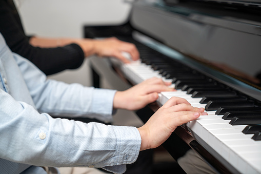 Selective focus on the kid finger playing grand piano. Teacher or instructor teach a boy on the class play melody. Close up hand of child. Music with piano. Education and learning concept.