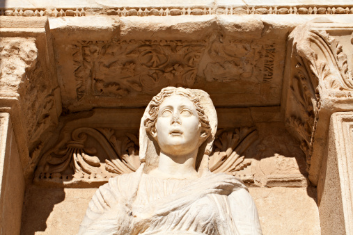 Ancient marble statue of a woman looks out under intricate archway copy space (statue is Sophia, Goddess of Wisdom, at the Celcus Library at Ephesus, Turkey)