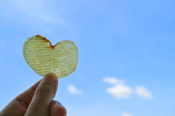 patatine a forma di cuore in mano di donna con sfondo cielo blu. - potato chip foto e immagini stock