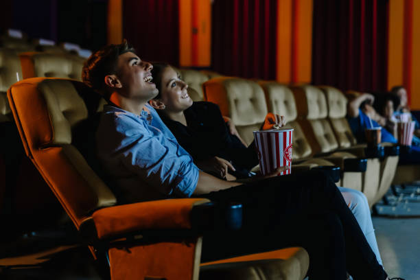 data di notte al cinema!. ritratto di giovane coppia felice seduta nell'auditorium del cinema che mangia popcorn e guarda film comici insieme. concetto di intrattenimento e solidarietà - date night foto e immagini stock