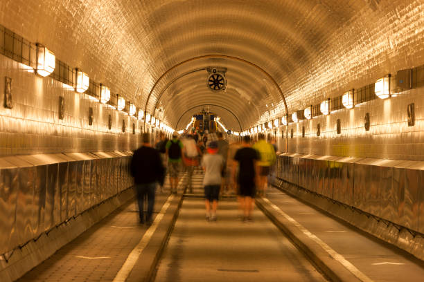 Old illuminated tunnel ( Elbtunnel) with sidewalks and road under River Elbe, blurred people, Hamburg, Germany.